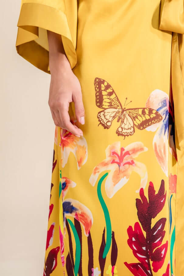 Close-up of Marigold Silk Satin Robe showcasing colorful butterfly and floral patterns on saffron yellow fabric.