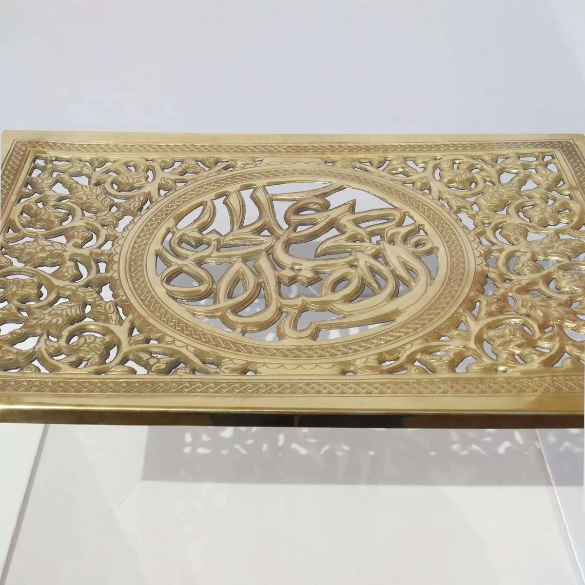 Engraved brass cover of a prayer mat box with Arabic calligraphy and intricate design details on a clear plexy body.