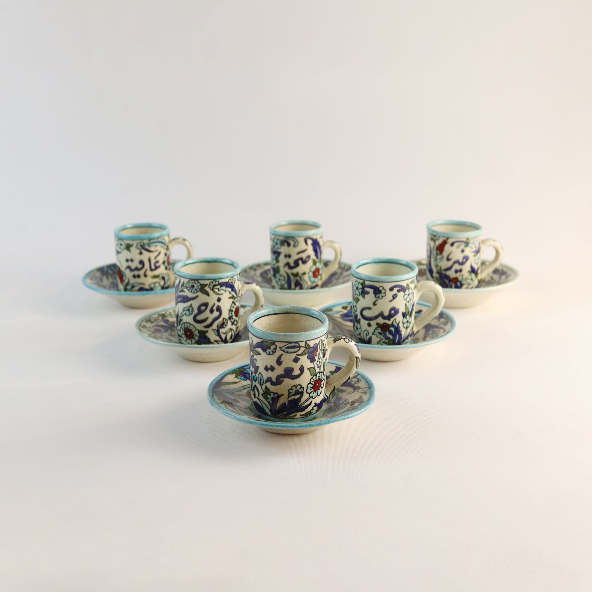 Set of ceramic cups and saucers with decorative patterns on a light gray background